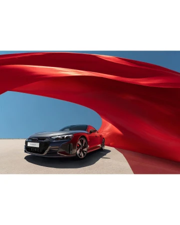 Red Audi e-tron GT car on a sandy surface with red fabric billowing in the background under a clear sky, promoting automotive design.