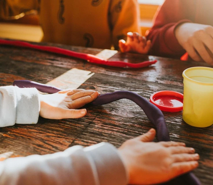 Children playing with colorful modeling clay on a wooden table indoors.  Kids craft project or creative play activity for entertainment.