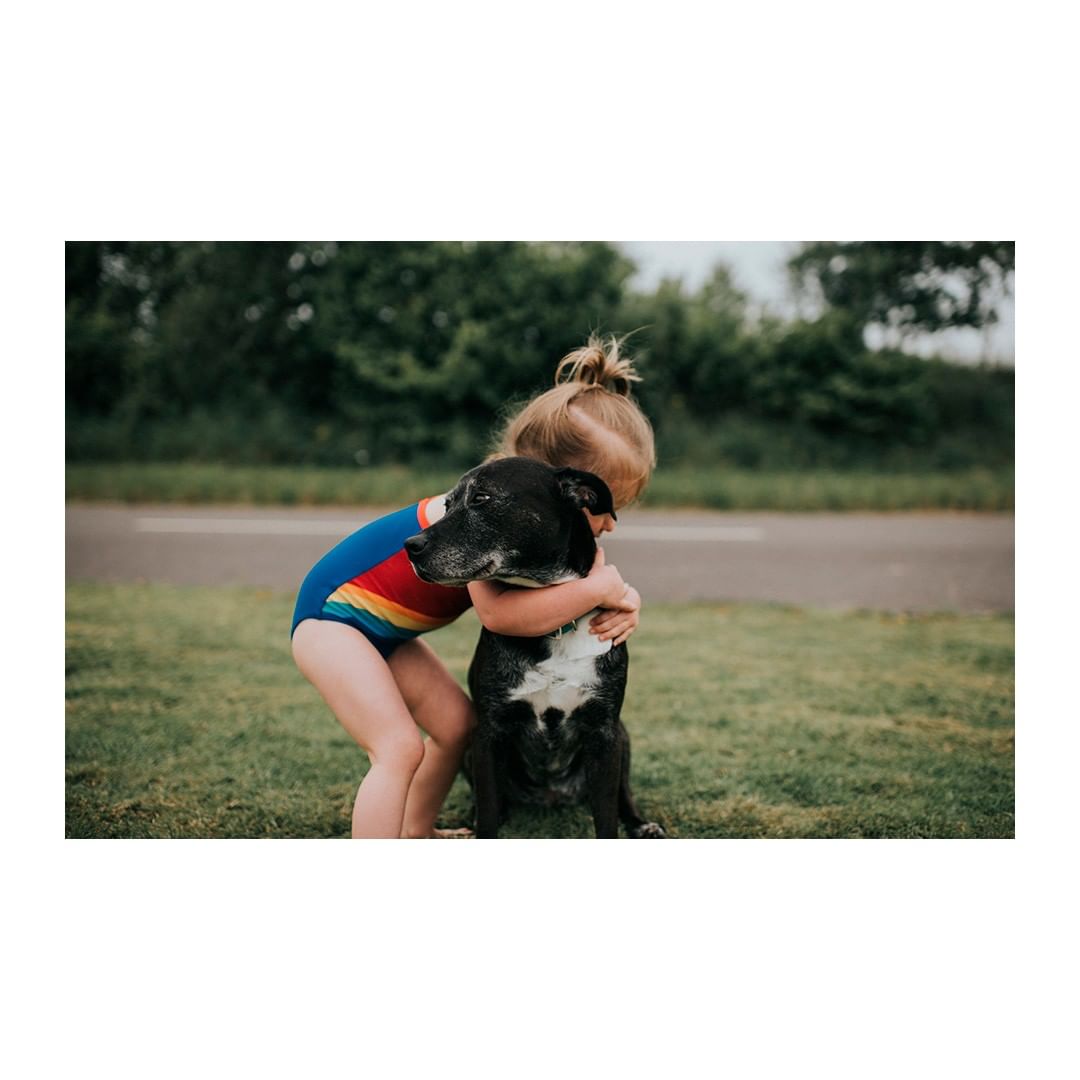 A young child embraces a black dog in a grassy outdoor setting on an overcast day, showcasing childhood innocence and animal friendship.