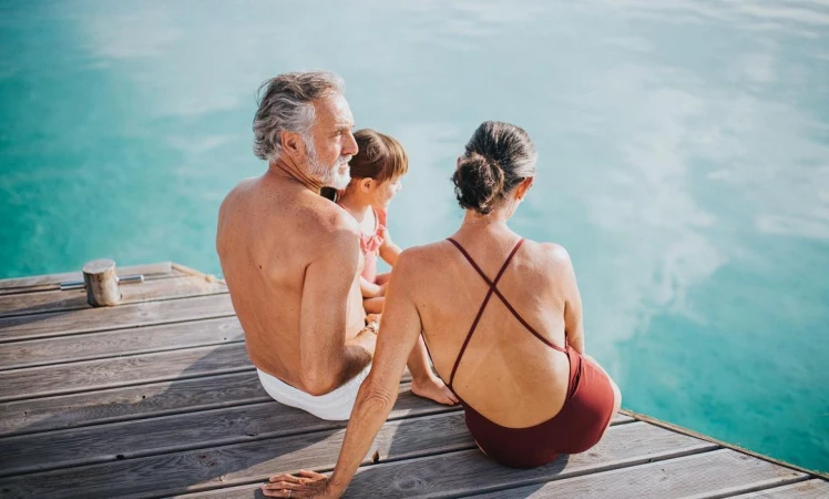 An older man, a child, and an older woman sitting together on a wooden dock overlooking turquoise water by photographer Catherine Falls.