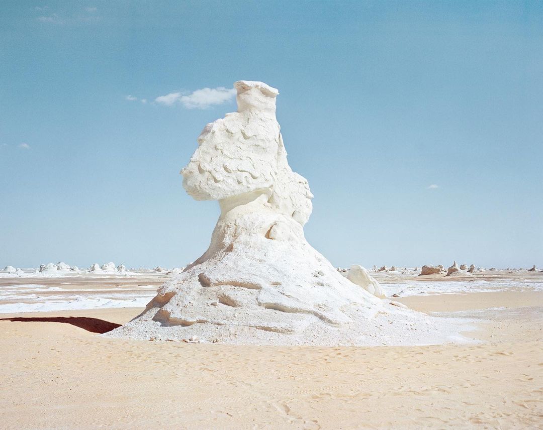 White rock formation in the desert against a pale blue sky. Arid landscape with unique natural rock formations and sandy ground.