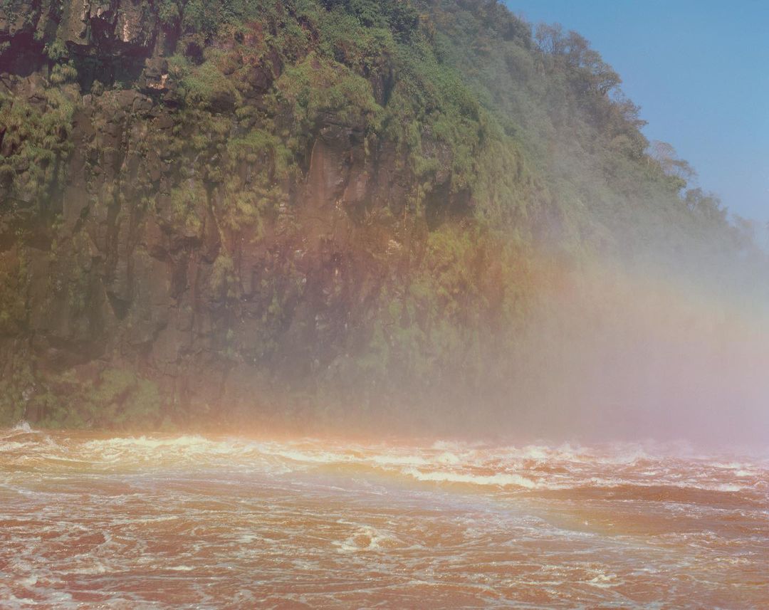 Scenic view of water cascading over rocks beneath lush vegetation, highlighting nature's power and the beauty of a natural landscape.