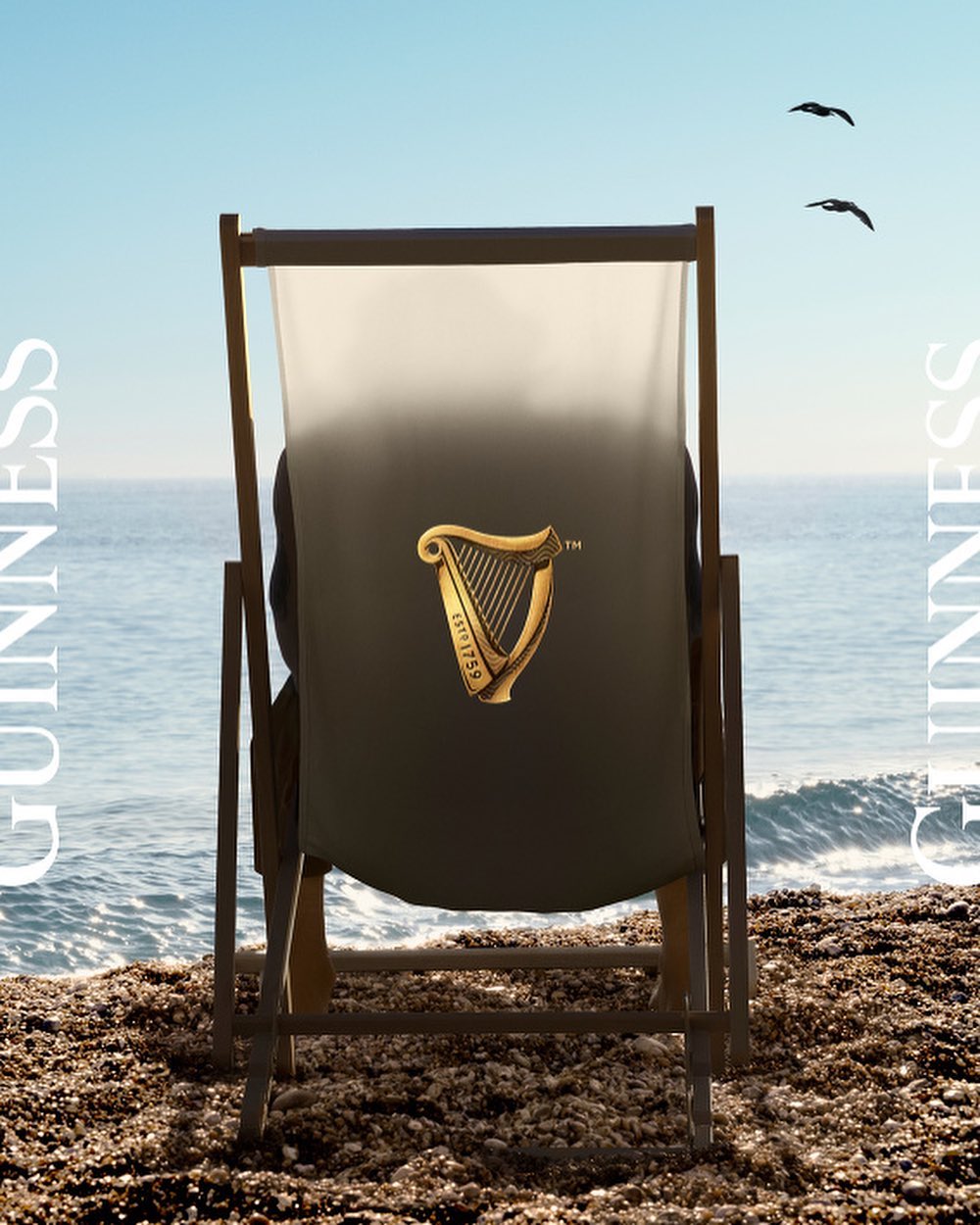 Guinness ad featuring a beach chair with the Guinness logo on a pebble beach, ocean backdrop, and birds flying in a blue sky.