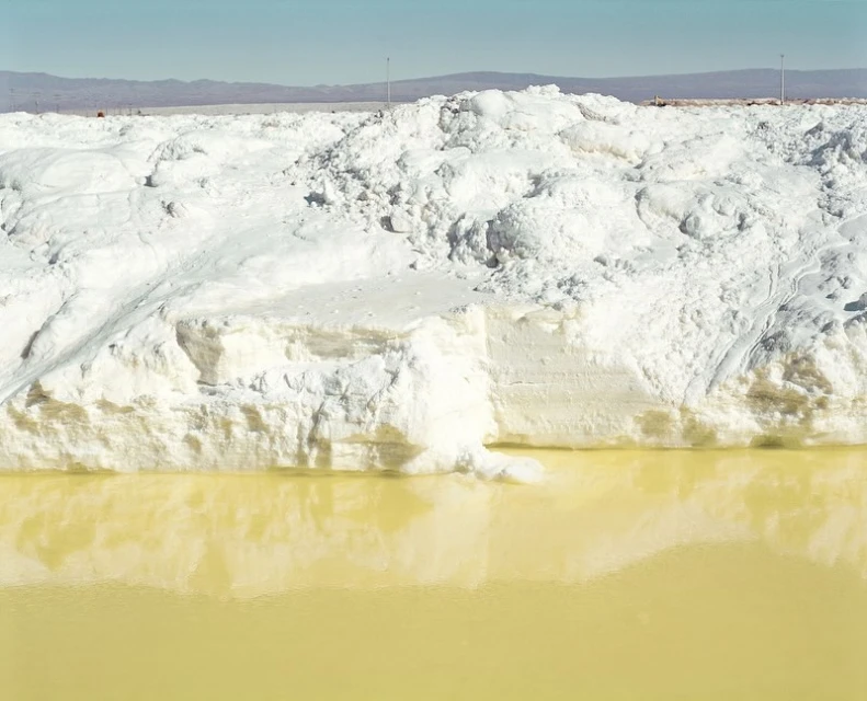 Expansive view of white mineral deposits and yellow-tinted water under a bright sky, creating a serene yet stark landscape.