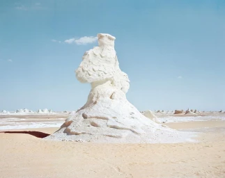 A towering white chalk rock formation stands in the middle of a vast desert landscape under a clear blue sky.