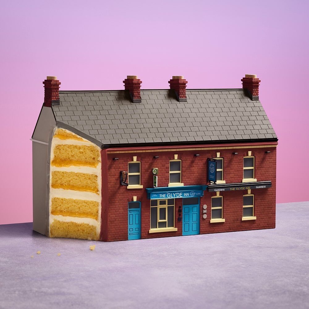 Novel architectural cake art depicting a detailed pub building facade featuring brickwork, windows, and signage against a pink background.