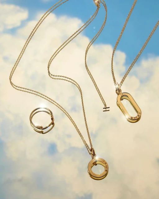 Elegant jewelry display featuring gold necklaces and a ring against a serene blue sky with soft, scattered clouds creating a dreamy backdrop.