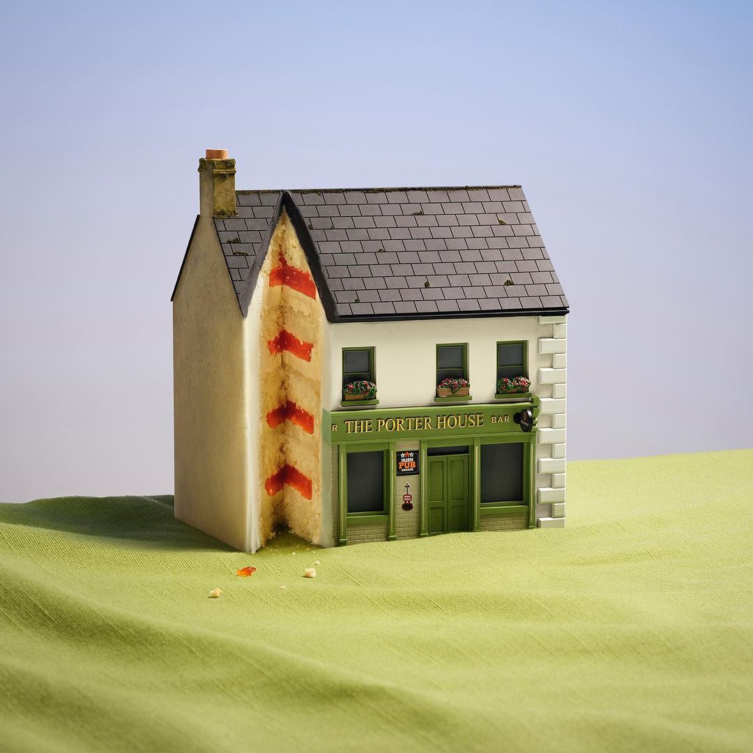 Whimsical miniature: A meticulously crafted cake resembling an Irish pub, with green facade and black roof, set on green fabric.