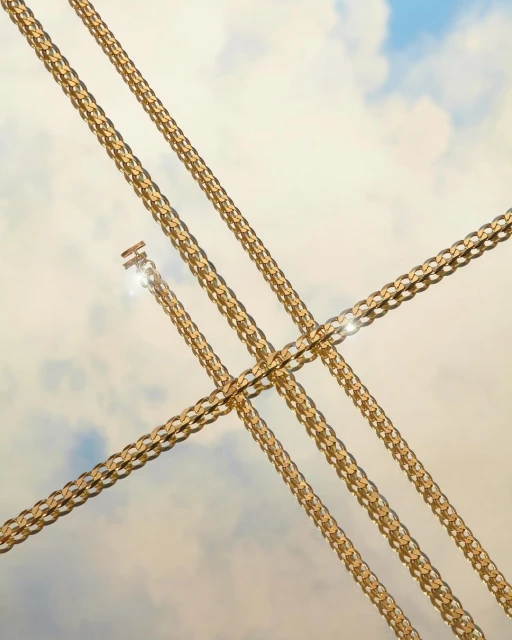 Four gold metal chains diagonally intersect in a symmetrical composition against a gradient blue and cream sky background. Close up.