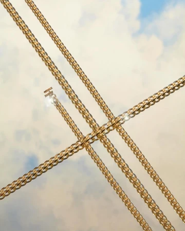 Four gold metal chains diagonally intersect in a symmetrical composition against a gradient blue and cream sky background. Close up.