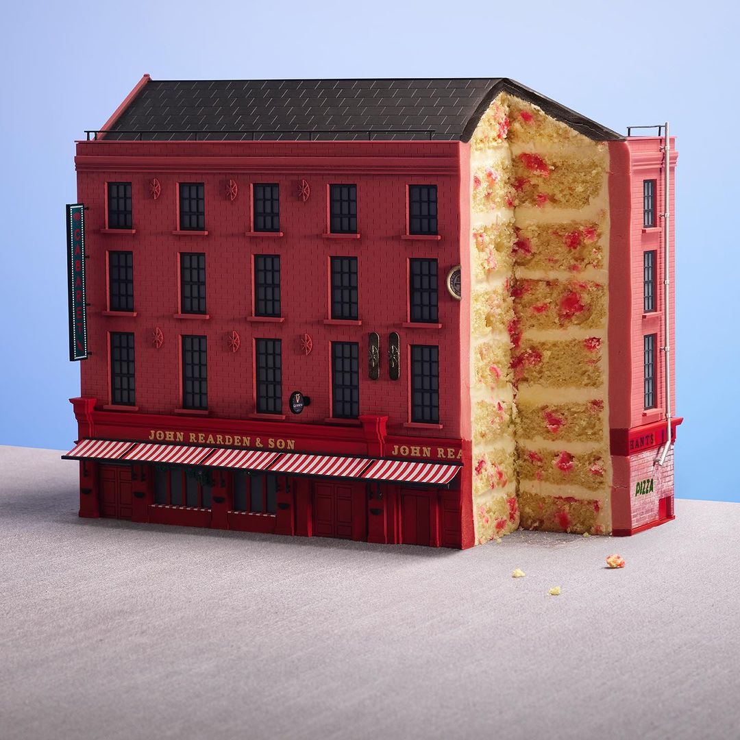 Novelty building-shaped cake, resembling a red brick structure, with a cross-section revealing sponge cake layers, and a blue background.