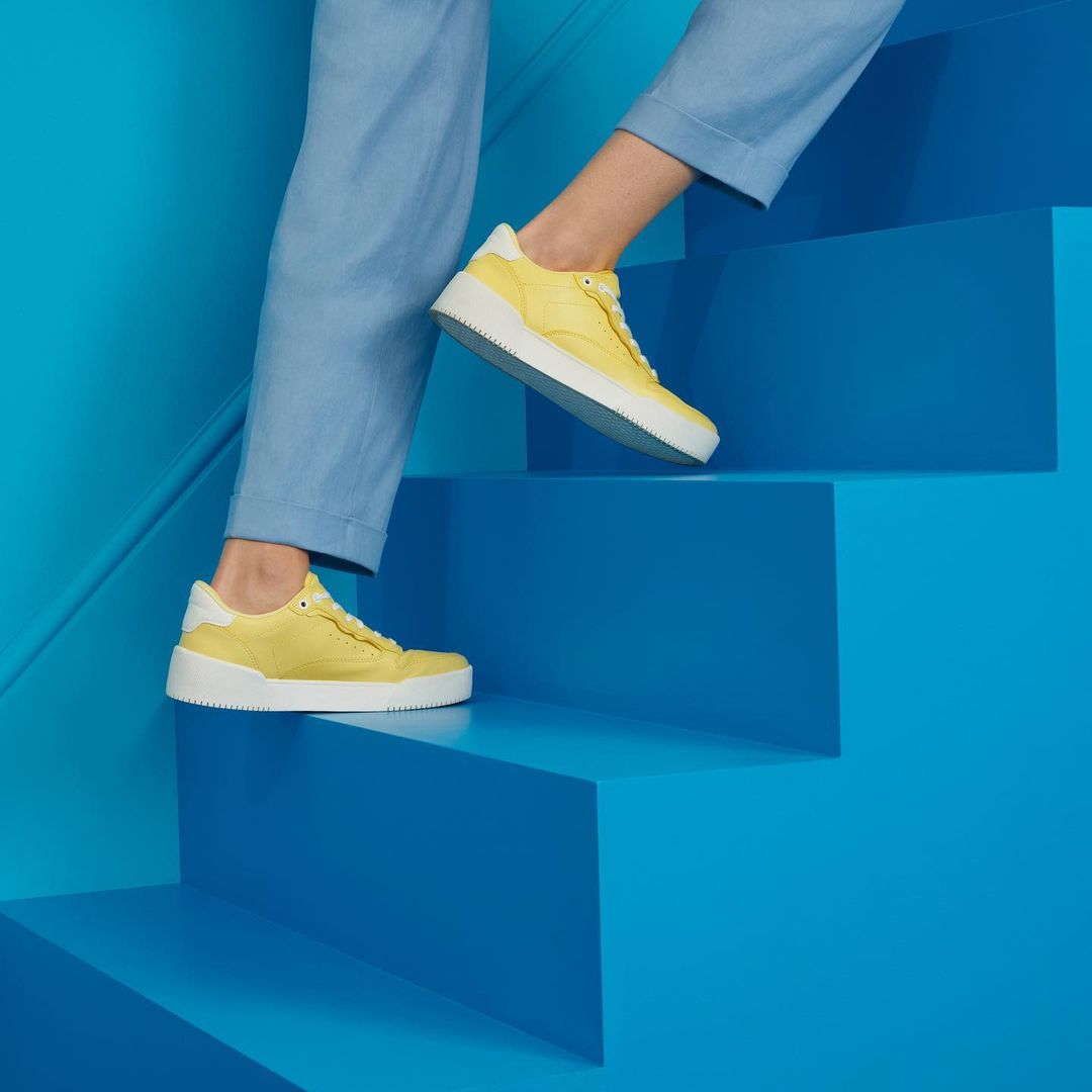 A person descends blue stairs wearing yellow and white sneakers and light blue trousers in a studio setting with bright lighting.