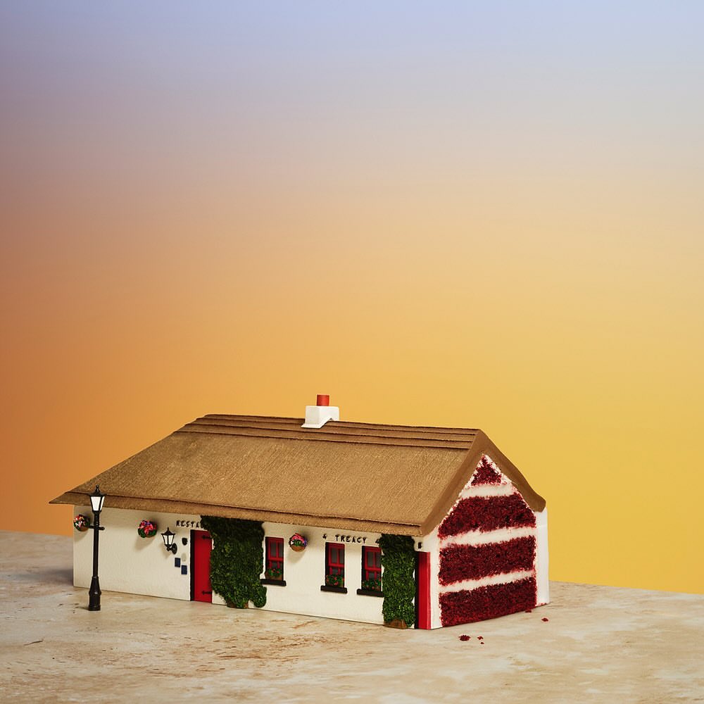 Whimsical miniature building crafted from cake stands against a smooth gradient backdrop, exuding a delightful and creative confectionary charm.