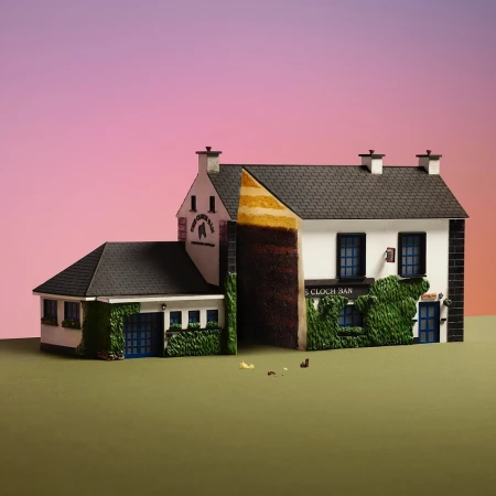Architectural model of a two-story white building with black shingled roof, green vine accents, and logo on a pink gradient backdrop.