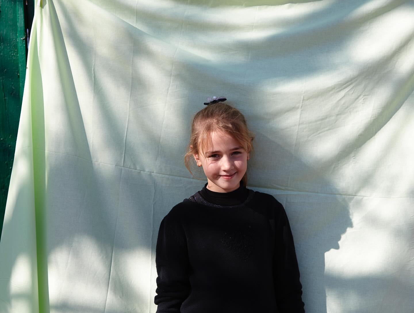 Young child in a black top standing in front of a draped pale green fabric backdrop photographed by Catherine Losing