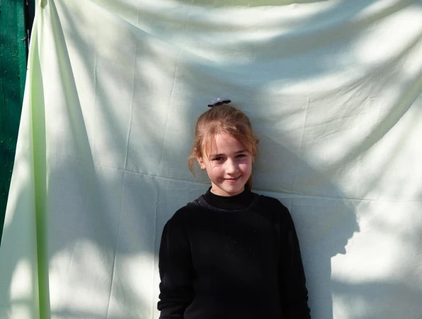 Young child in a black top standing in front of a draped pale green fabric backdrop photographed by Catherine Losing