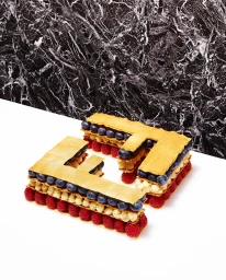 Letter-shaped layered pastry with raspberries and blueberries set against white surface and black marble wall