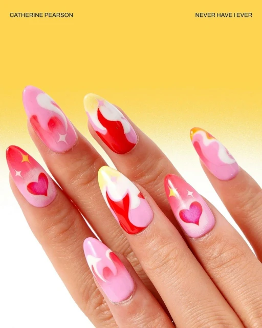 Close-up of a manicured hand showcasing long, almond-shaped nails with pink, red, yellow, and white abstract flame and heart designs.