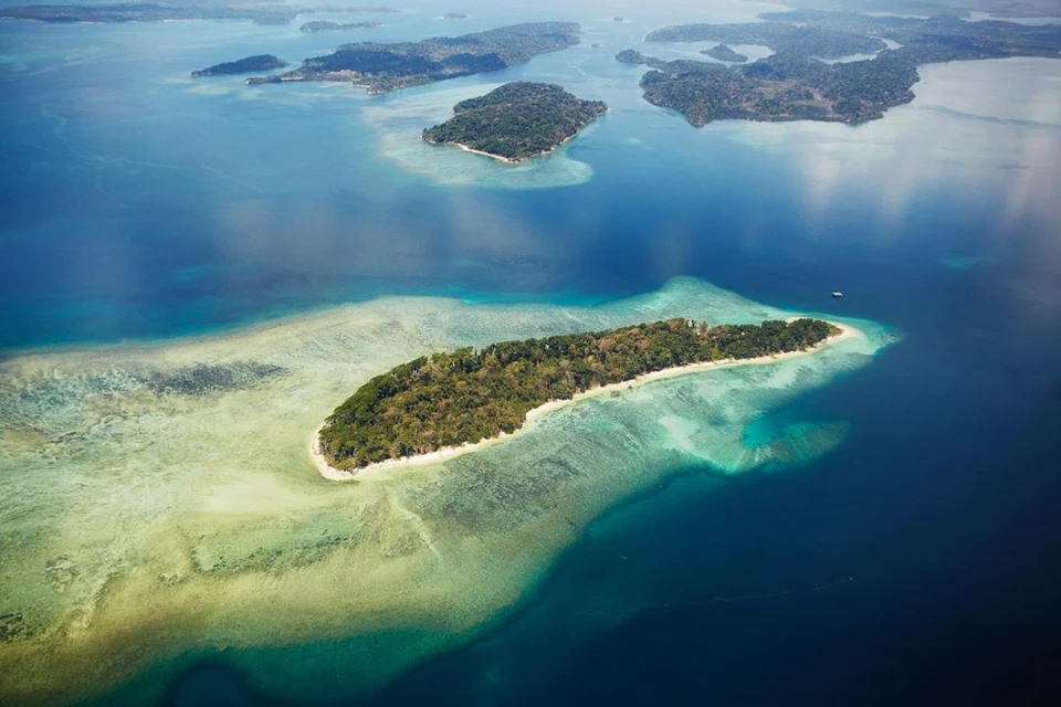 Aerial view of a tropical island with lush greenery, surrounded by clear turquoise water and coral reefs, creating a stunning seascape.