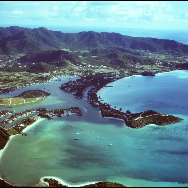 Aerial view of a tropical coastline featuring turquoise water, sandy beaches, and lush green mountains in the background on a sunny day.