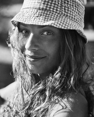 Close-up black and white portrait of a smiling woman wearing a patterned bucket hat outdoors.