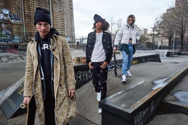Three young models holding skateboards posing in a concrete skate park wearing streetwear and outerwear