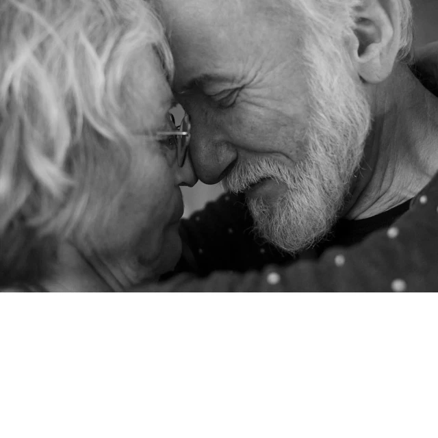 A close-up, black and white image capturing an elderly couple in a tender moment, their foreheads touching and eyes closed, conveying intimacy.