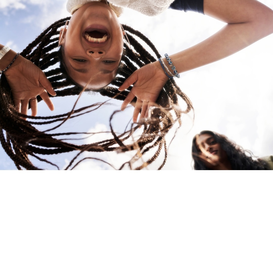 Two women smile in an eye-level medium shot; one woman is up close with her head inverted and braids framing her face.