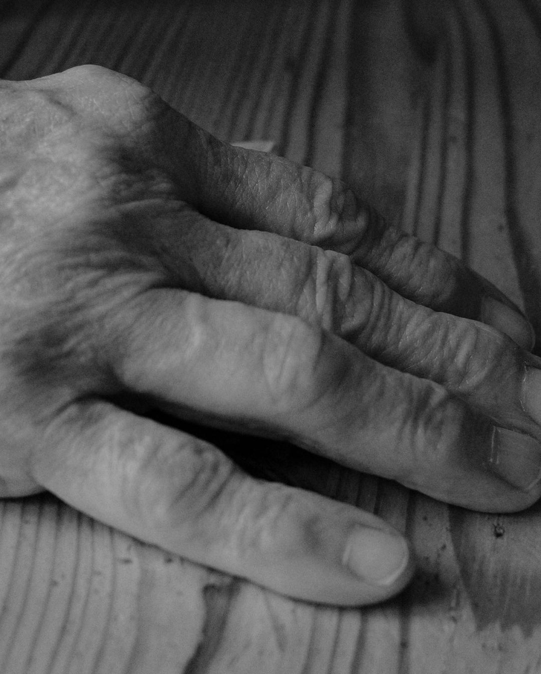 Detailed black and white close-up shot of an elderly person's hand resting on a light-colored wooden surface, highlighting texture.