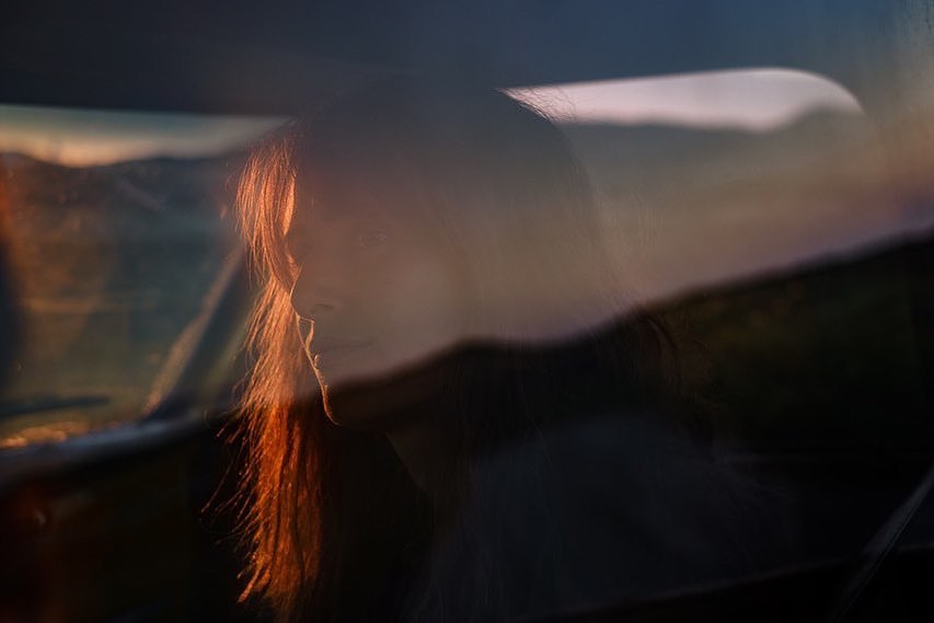 Woman inside car during sunset.  Adult female with long reddish-brown hair. Travel by car on open road with beautiful scenery.