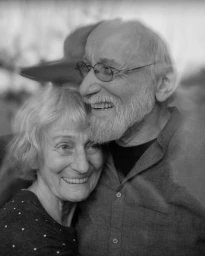 Black and white portrait of an elderly couple smiling, embracing closely, with an overlaid translucent reflection.