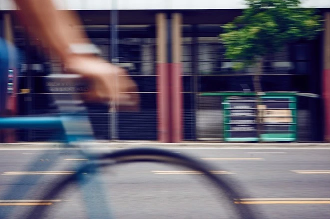 Motion-blurred photograph of a bicycle wheel and handlebars passing a city street by photographer Cecil Arp.