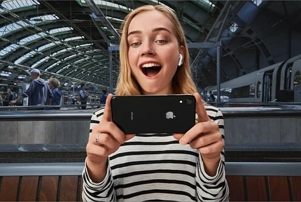 Blonde woman wearing striped sweater holding a black smartphone horizontally inside a train station