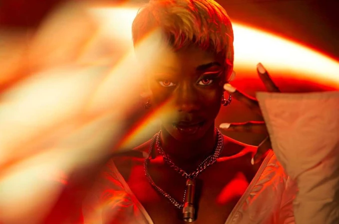 Portrait of a black woman with short blonde-tipped hair posing with a silver chain necklace in a neon-lit environment