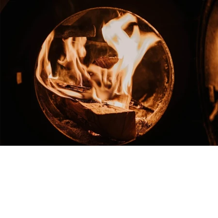 Close-up of bright orange flames and burning logs inside a round metal wood-burning stove