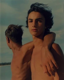 Two young men standing outdoors with arms draped over shoulders against an open sky background