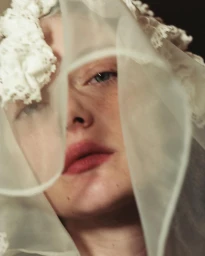Close-up portrait of a woman wearing an intricate white lace headpiece and sheer veil by Cécile Smetana