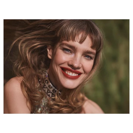 Close-up portrait of a smiling woman with long blonde hair blowing in the wind wearing a beaded top and red lipstick