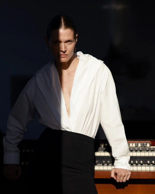 Indoor portrait of an adult woman in a white shirt and black skirt posing near a vintage organ with dramatic, contrasting lighting.
