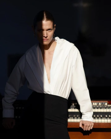 Indoor portrait of an adult woman in a white shirt and black skirt posing near a vintage organ with dramatic, contrasting lighting.