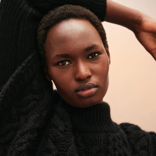 Close-up studio portrait of an African woman wearing a knitted black turtleneck sweater against a neutral peach background. Fashion.