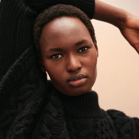 Close-up studio portrait of an African woman wearing a knitted black turtleneck sweater against a neutral peach background. Fashion.