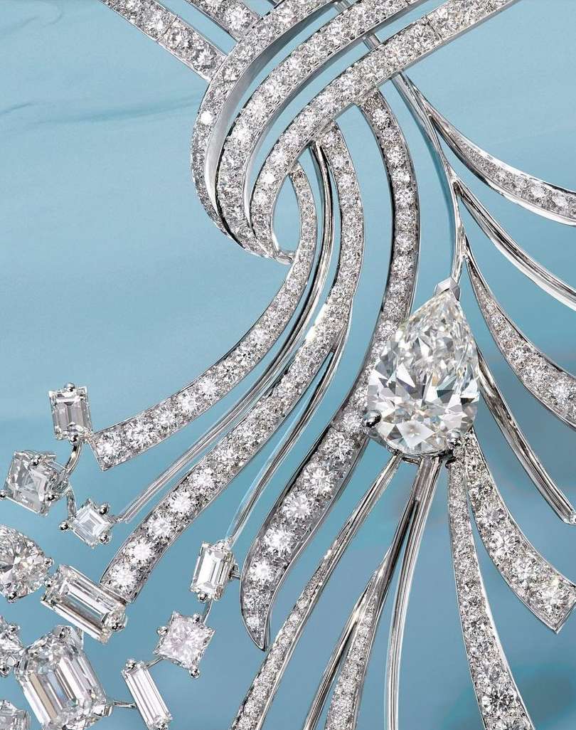 Close-up of a diamond necklace featuring pave diamonds and a pear-shaped diamond pendant against a soft blue background.