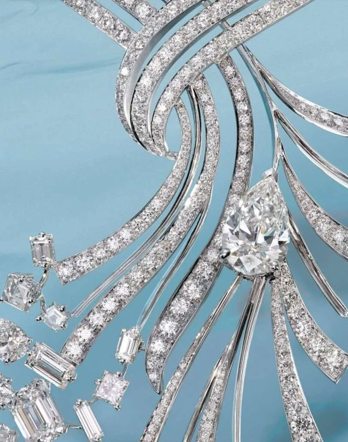 Close-up of a diamond necklace featuring pave diamonds and a pear-shaped diamond pendant against a soft blue background.