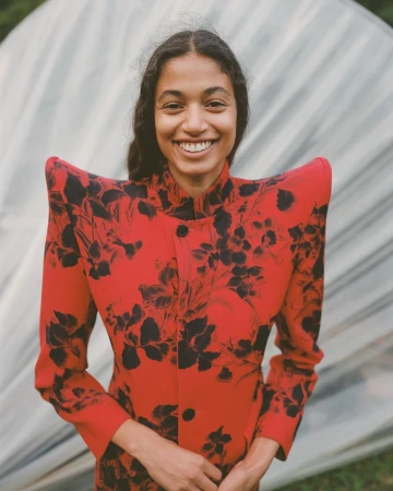Portrait of a smiling woman wearing a striking red structured-shoulder jacket with black floral print, photographed by Cedric Bihr