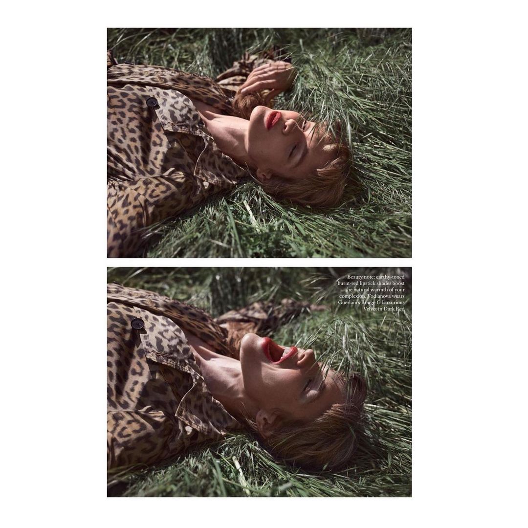 Woman in a leopard-print coat lies in tall green grass, eyes closed, mouth open, red lipstick, sunlit, outdoor fashion editorial.