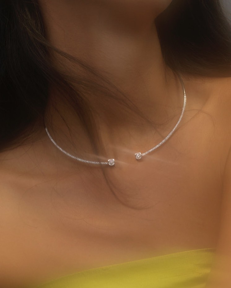Close-up of an adult female model wearing a silver choker necklace, showcasing fashion and beauty in a softly lit studio environment.