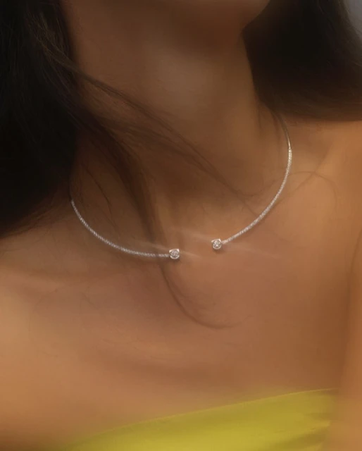 Close-up of an adult female model wearing a silver choker necklace, showcasing fashion and beauty in a softly lit studio environment.