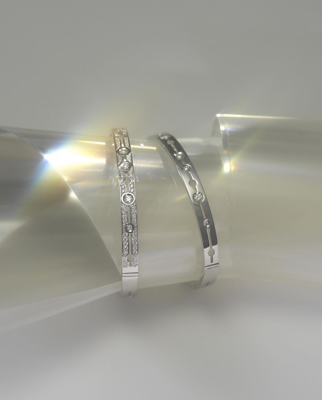 Close-up of two silver-tone bangles with gemstone accents on a reflective surface with a soft, diffused lighting.