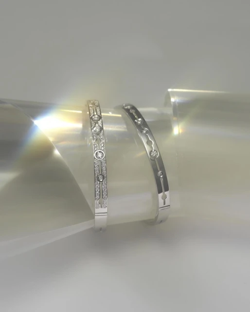 Close-up of two silver-tone bangles with gemstone accents on a reflective surface with a soft, diffused lighting.